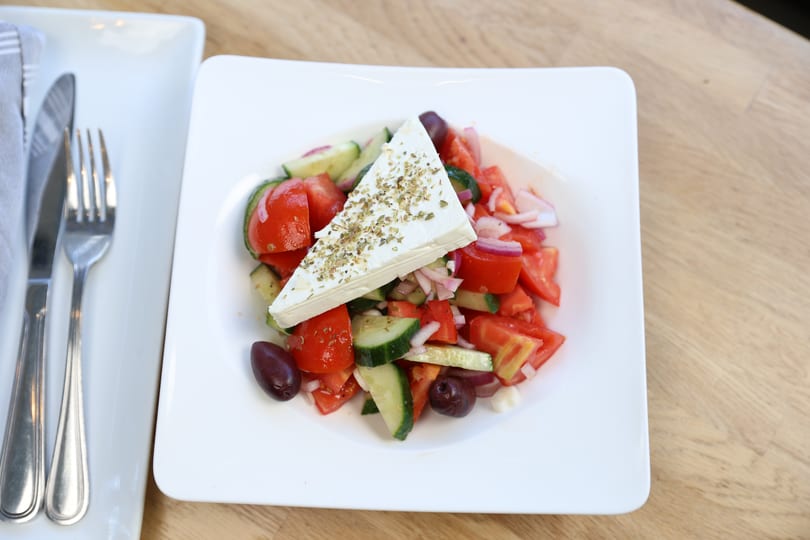 A fresh Greek salad with tomatoes, cucumbers, red onions, olives, and a large feta cheese block.