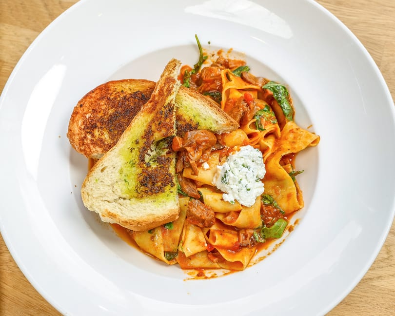 Pappardelle pasta with meat sauce, spinach, ricotta, and two slices of garlic bread.