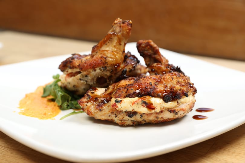Grilled chicken wings and stuffed chicken breast with sauce and greens on a white plate.