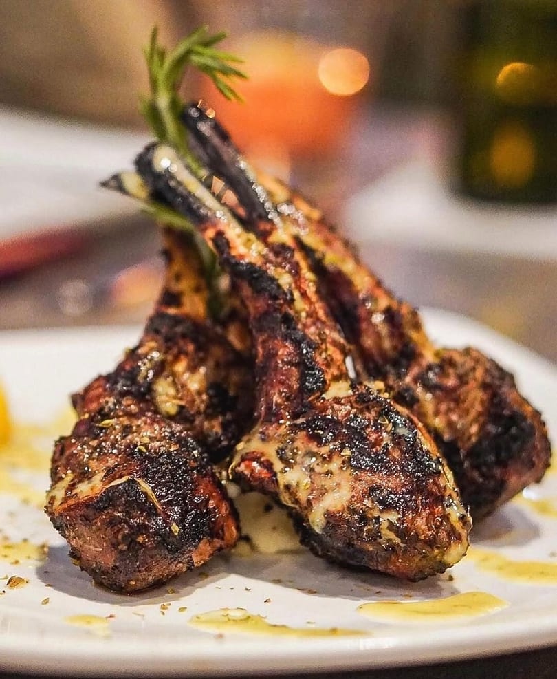 Grilled lamb chops with herbs and a creamy sauce, served on a white plate.