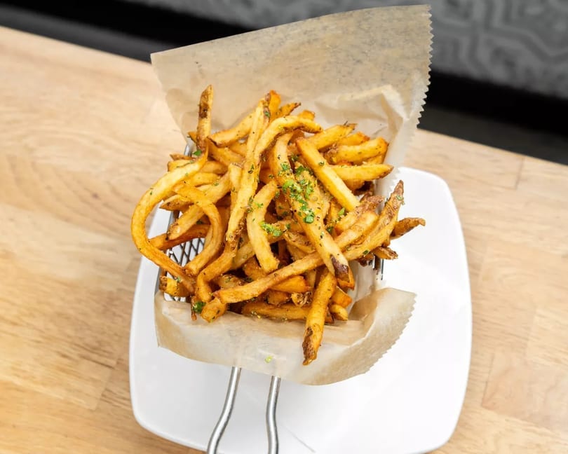 Crispy golden french fries seasoned with herbs, served in a metal basket lined with parchment paper.