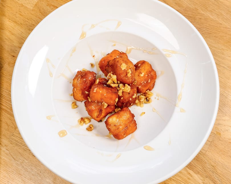 Golden-brown fried dough pastries drizzled with honey and sprinkled with chopped walnuts on a white plate.