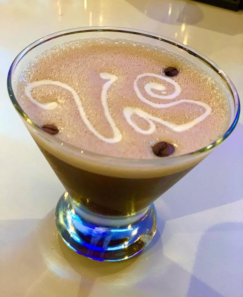 Espresso martini with foam art and coffee beans in a martini glass with a blue-lit base.