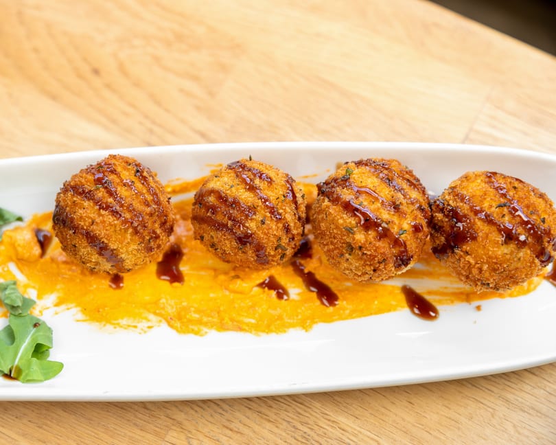 Four golden-brown arancini balls drizzled with dark sauce, served on orange puree with arugula.