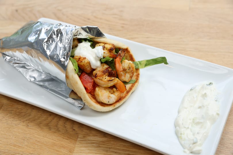Shrimp pita wrap with lettuce, tomatoes, and tzatziki sauce, served on a white plate.