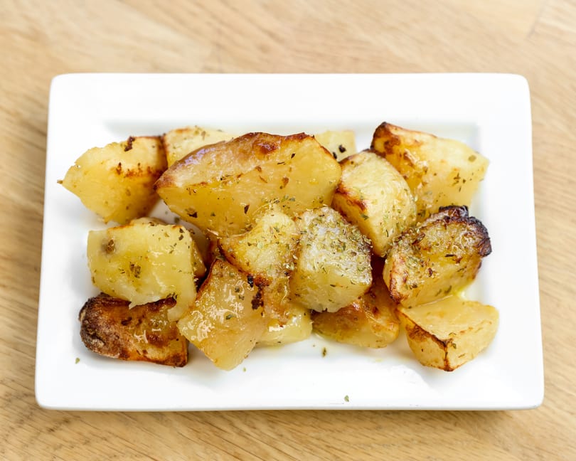 Golden roasted potatoes seasoned with herbs, served on a white rectangular plate.